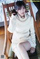 A woman sitting in a chair wearing a white sweater.