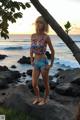 A woman standing on a rock by the ocean at sunset.