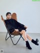 A woman sitting in a chair wearing a black dress and black boots.