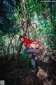 A woman in a red hooded outfit is posing in the woods.