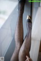 A woman wearing black stockings and high heels leaning against a window.